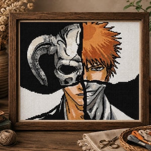 Puede incluir: Un bordado en punto de cruz enmarcado que muestra el retrato dividido de un personaje con cabello naranja puntiagudo en un lado y una máscara de calavera blanca con cuernos en el otro. El diseño utiliza un fondo de alto contraste.