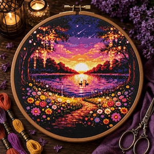Pode incluir: Um bastidor de bordado circular de madeira contendo um padrão de ponto cruz de um pôr do sol sobre um lago. A cena apresenta um sol brilhante, nuvens roxas e laranjas, dois cisnes na água e um primeiro plano cheio de flores coloridas.
