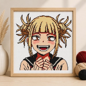 May include: A square framed cross-stitch embroidery featuring a pixel art style portrait of a character with blonde hair styled in two messy buns, large orange eyes, and a wide smiling expression, wearing a dark collared garment with red accents.
