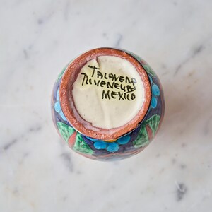 May include: A small, round, hand-painted ceramic vase with a dark blue background and colorful floral designs. The rim is brown, and the interior is white. The bottom of the vase has the text "Talavera, Mexico".