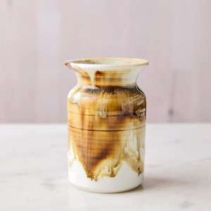May include: A handcrafted ceramic vase with a unique, organic design. The vase features a white base that transitions to shades of brown and tan, with a dripped glaze effect. The top rim is a lighter color, creating a striking contrast.