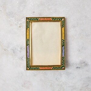 May include: A rectangular metal picture frame featuring a decorative border of tiny, colorful floral mosaic tiles in shades of orange, yellow, green, and purple, surrounding a plain, light-colored rectangular insert within a gold-toned metal edge.
