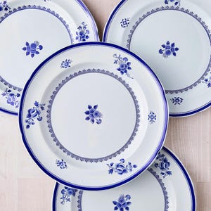 May include: White ceramic plates with a blue floral design. The plates have a blue border and a central floral motif. The design includes detailed floral patterns and decorative elements. The plates are arranged on a light-colored surface.