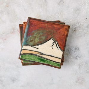 May include: A set of three ceramic mugs with a speckled, matte finish. The mugs are in shades of cream, light gray, and dark gray. Each mug has a simple, minimalist design and a rounded handle. The mugs are stacked on top of each other.