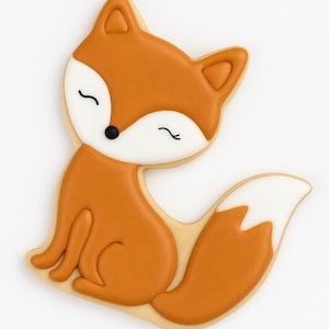 May include: A decorated fox-shaped cookie with orange icing and a white tail. The fox has a black nose and closed eyes, with a light-colored cookie base. The cookie is a whimsical treat.