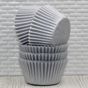 May include: A stack of silver cupcake liners. The liners are made of paper and have a fluted design.