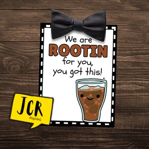 May include: A white card with black and white dashed borders and a black bow tie at the top. The card says "We are ROOTIN for you, you got this!" and has a cartoon image of a glass of root beer with ice cubes and a smiling face.