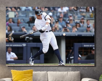 May include: A baseball player in a pinstriped uniform swings a bat, wearing a white cap with a blue logo. The player is in a stadium with a crowd of spectators in the background.