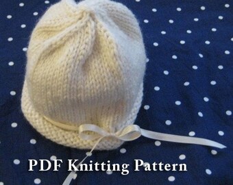 May include: A white knitted baby hat with a white satin ribbon tied around the brim. The hat is on a blue background with white polka dots. PDF Knitting Pattern.