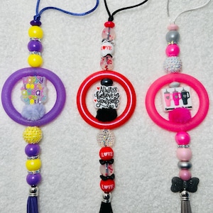 May include: Three colorful beaded car charms with a ring and tassel. The charms feature the phrases "Happy Looks Good On You", "Always Believe In Yourself", and "Sweet Dreams".