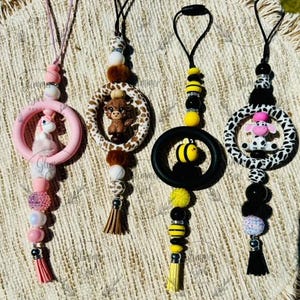 May include: Four colorful silicone baby teethers with different animal characters. Each teether has a round shape with a beaded chain and a tassel. The animals include a unicorn, a cow, a bee, and a giraffe.
