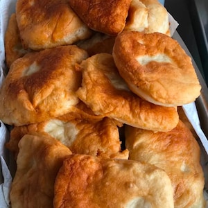 May include: A pile of golden brown, deep-fried dough balls, likely a type of bread or pastry, in a white paper-lined container.