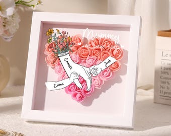 Può includere: Cornice bianca con un cuore di rose rosa e pesca con le parole "Mummy We Love You" e tre nomi, "Emmett", "Emma" e "Jack" scritti sulle mani.