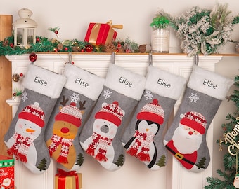 May include: Five gray Christmas stockings with white fur trim, each personalized with the name "Elise". The stockings feature different festive characters: a snowman, a reindeer, a polar bear, a penguin, and Santa Claus.