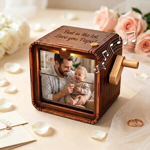 Peut inclure: Une boîte à musique carrée en bois avec une finition brun foncé et une manivelle sur le côté. Le dessus est gravé avec le texte Best in the lot. Love you Papa! L'avant présente une photographie d'un adulte tenant un bébé, avec des notes de musique.