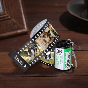 May include: A black and white film strip keychain with a black and white photo of a dog and the name "Lucas" printed on it. The keychain is attached to a black and green film canister with the text "X-TRA 400 FILM FOR COLOR PRINTS 36 CH135 SUPER 400-36-400/27 FUJIFILM PROCESS DXF CN16 C-41" printed on it.