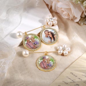Puede incluir: Broches dorados con marcos de fotos redondos, adornados con pedrería. Cada broche presenta un acento de perla y un alfiler. Algunos broches tienen un grupo de perlas en forma de flor. Las fotos muestran parejas y familiares.