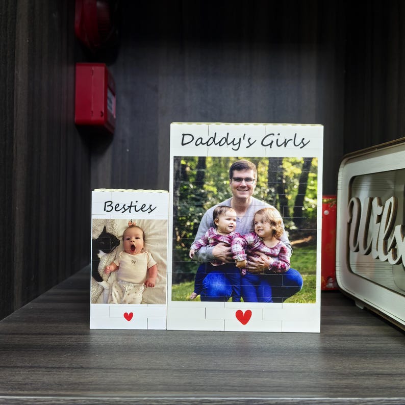 Puede incluir: Dos expositores de fotos de bloques de madera. Uno dice "Besties" con una foto de beb&eacute; y un coraz&oacute;n. El otro dice "Daddy's Girls" con una foto de un hombre y dos ni&ntilde;os y un coraz&oacute;n. Los bloques est&aacute;n sobre una superficie oscura.