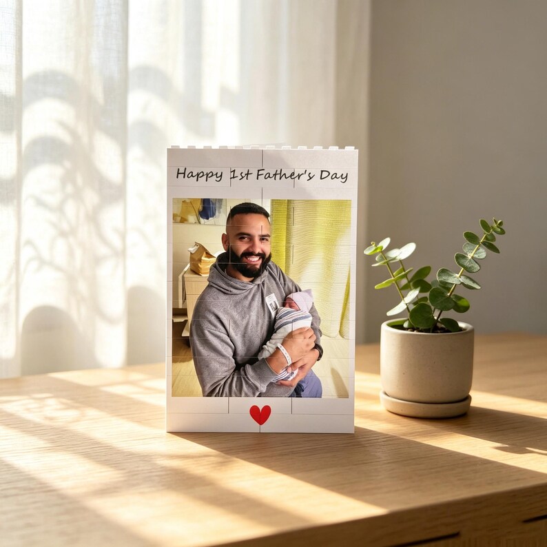 Puede incluir: Un marco de fotos de bloque blanco con el texto "Happy 1st Father's Day" y un coraz&oacute;n rojo. El marco contiene una foto de un hombre sosteniendo a un beb&eacute;. Una peque&ntilde;a planta en maceta est&aacute; a la derecha.