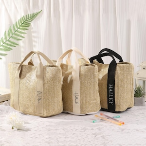 Peut inclure: Trois sacs fourre-tout en paille tress&eacute;e avec des anses en tissu. Un sac a une anse noire et le nom "Hailey" imprim&eacute; sur une bande verticale. Les deux autres sacs ont des anses beiges.
