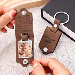May include: Brown leather keychain with a photo frame and a calendar. The calendar shows the date "July 31, 2024" and the text "The day you became my daddy". The other side of the keychain has the text "Love you daddy".