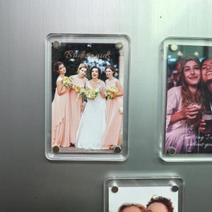 Könnte beinhalten: Ein rechteckiger, klarer Acrylmagnet mit einem Foto einer Braut und ihrer Brautjungfern. Die Brautjungfern tragen pfirsichfarbene Kleider und halten Blumensträuße. Die Braut trägt ein weißes Kleid. Das Wort "Bridesmaids" steht in Schreibschrift oben.