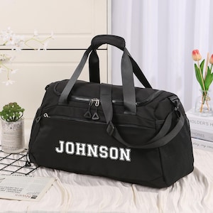 Peut inclure: Un sac de sport noir avec le nom "JOHNSON" en lettres blanches. Le sac est doté d'une poignée supérieure, d'une bandoulière et de plusieurs compartiments zippés. Une poche en filet est visible sur le côté. Le sac est posé sur une surface blanche.