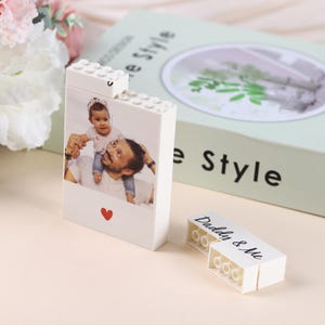 Puede incluir: Un bloque blanco estilo Lego con una foto de un padre y un ni&ntilde;o, un coraz&oacute;n rojo y el texto "Daddy & Me". Es un regalo personalizado, posiblemente un marco de fotos o un objeto decorativo.