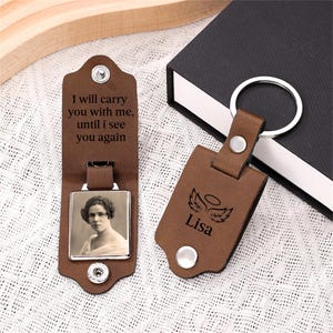 May include: Brown leather keyring with a silver photo frame and a small photo of a woman. The keyring has the text "I will carry you with me, until I see you again" and "Lisa" with angel wings.
