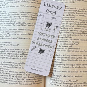May include: A bookmark with a library card design, featuring the text "The Tortured Readers Department." It includes spaces for date and title, along with illustrations of a typewriter, feather, and envelope. The words "Book Lover" are at the bottom.