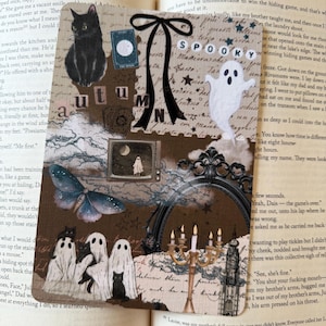 May include: A rectangular bookmark featuring a collage of autumn and Halloween imagery, including a black cat, a white ghost, a moth, a candelabra, and a mirror. The design incorporates the text "SPOOKY" and "autumn" against a vintage paper background.