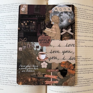 May include: A rectangular bookmark featuring a collage of autumn-themed imagery, including a full moon with the text M, O, O, N, a person reading, a cup of coffee, a black cat, and text reading Delicious Apple Cider and I'm so glad I live in a world where there are Octobers.