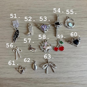 May include: A selection of silver charms, featuring a raven, cowboy boot, winged heart, cross, crescent moon, bow, envelope, floral wreath, cherries, football, and heart. Ideal for jewellery making or crafting projects.