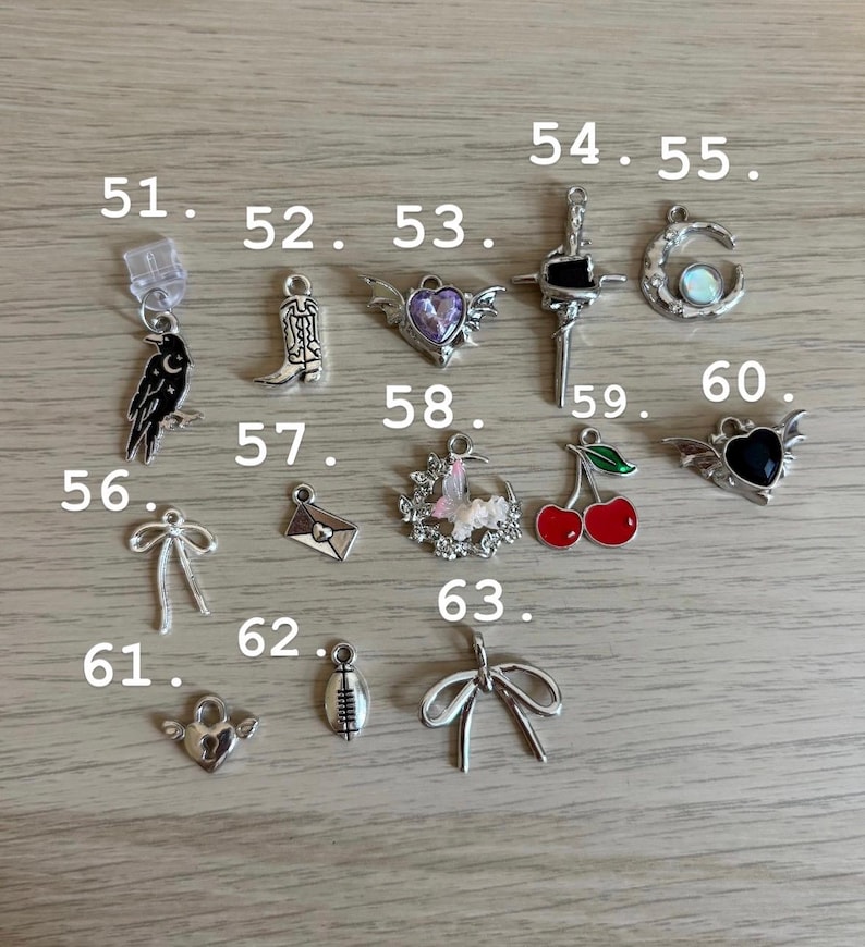 May include: A selection of silver charms, featuring a raven, cowboy boot, winged heart, cross, crescent moon, bow, envelope, floral wreath, cherries, football, and heart. Ideal for jewellery making or crafting projects.