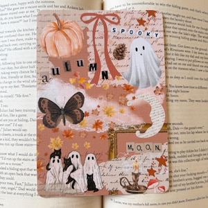 May include: A rectangular bookmark featuring a collage of autumn and Halloween imagery, including a pumpkin, a ghost, a butterfly, black cats, and a candle. The design incorporates text elements reading "autumn," "spooky," and "M, O, O, N," set against a background of script, leaves, and a red ribbon.