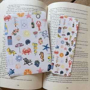 May include: Two square coasters with a summer theme, featuring illustrations of crabs, starfish, and beach umbrellas. The coasters are placed on an open book.