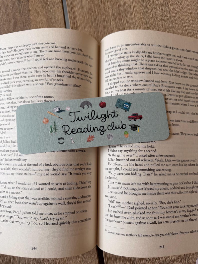 May include: A rectangular light blue bookmark featuring the text "Twilight Reading club" in black script. The design includes small illustrations of a baseball cap, bat, apple, red truck, graduation cap, trees, leaves, and other icons.