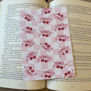 May include: A pink and white chequered pattern featuring illustrations of cherries and bows. The cherries are red, and the bows are pink. The design is on a white background.