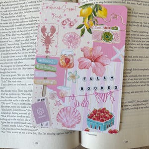 May include: A pink and white bookmark featuring beach-themed illustrations such as a lobster, seashells, and a camera. The text "Emotional Support Kindle" and "FULLY BOOKED" are also present.