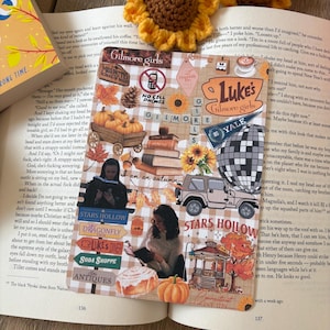 May include: A bookmark with a collage of autumn-themed stickers and illustrations, including pumpkins, sunflowers, and text from the show "Gilmore Girls." The bookmark is on an open book with a crocheted sunflower.