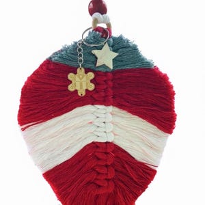 May include: A handmade macrame wall hanging in red, white, and teal. A wooden star and a charm with a floral design hang from a keychain attached to the macrame. A red bead and a white cord are at the top.