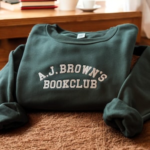May include: A dark green sweatshirt with the text "A.J. BROWN'S BOOKCLUB" embroidered in white on the front.