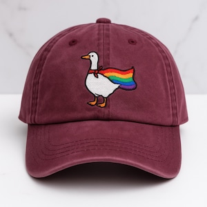 May include: A maroon baseball cap with an embroidered white goose wearing a rainbow cape.