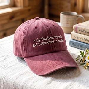May include: A maroon baseball cap featuring the white embroidered text "only the best friends get promoted to auntie" on the front panel. The cap has a structured crown, a curved brim with visible stitching, and a button at the top center.