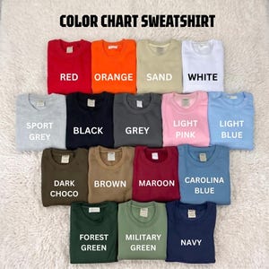 May include: A color chart of crewneck sweatshirts featuring the text COLOR CHART SWEATSHIRT. The collection includes red, orange, sand, white, sport grey, black, grey, light pink, light blue, dark choco, brown, maroon, carolina blue, forest green, military green, and navy.