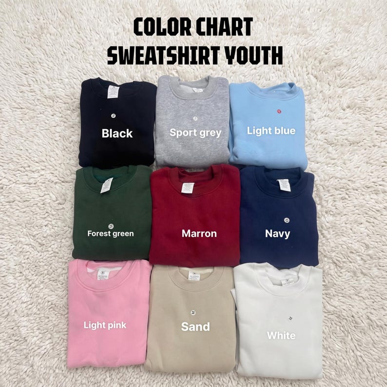 May include: A color chart for youth sweatshirts featuring nine folded crewneck sweaters in black, sport grey, light blue, forest green, maroon, navy, light pink, sand, and white. The text COLOR CHART SWEATSHIRT YOUTH is displayed at the top.