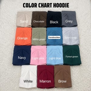 May include: A color chart for hoodies featuring fifteen folded fabric squares in various colors including sand, chocolate, black, grey, orange, military green, Carolina blue, sport grey, navy, light pink, light blue, forest green, white, maroon, and brown.