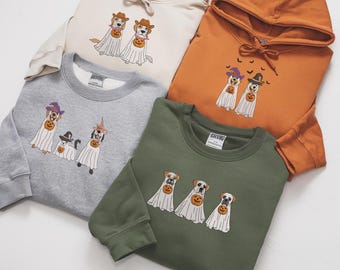 May include: A collection of four sweatshirts and hoodies in cream, orange, gray, and olive green. Each garment features an embroidered graphic of dogs dressed as ghosts wearing hats and holding pumpkins for the Halloween season.