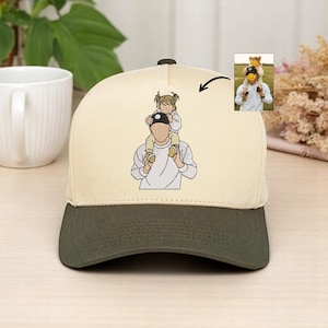 May include: A beige and olive green baseball cap with an embroidered design. The design depicts a person carrying a child on their shoulders. A small photo of the same scene is in the upper right corner.