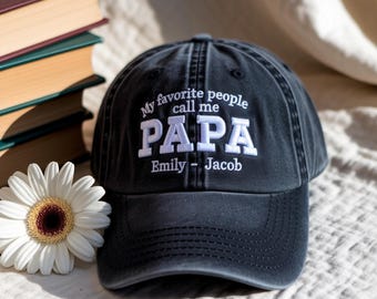 May include: A charcoal gray baseball cap featuring white embroidered text that reads My favorite people call me PAPA followed by the names Emily - Jacob. The cap has a curved brim and a structured crown with a button at the top center.